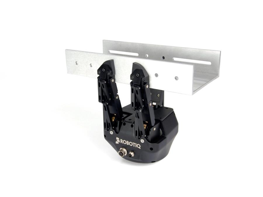 A black three finger robotic hand holds a silver piece of equipment.