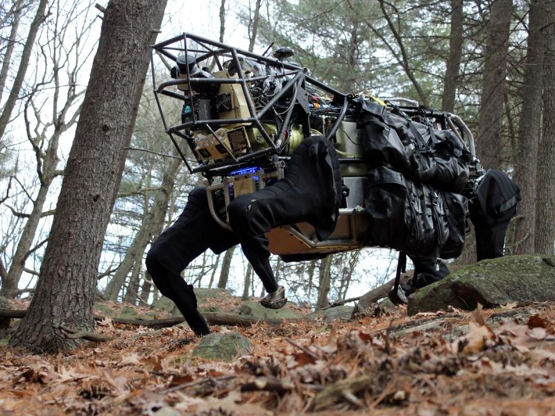 A very large black quadruped robot in the woods.