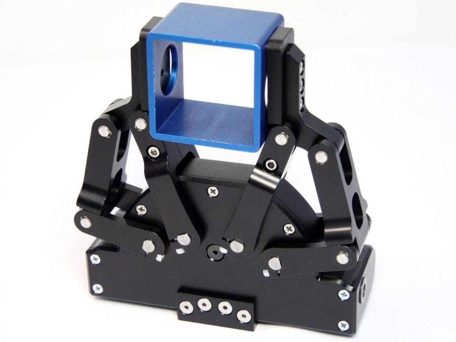 A two finger black piece holds a blue cube.