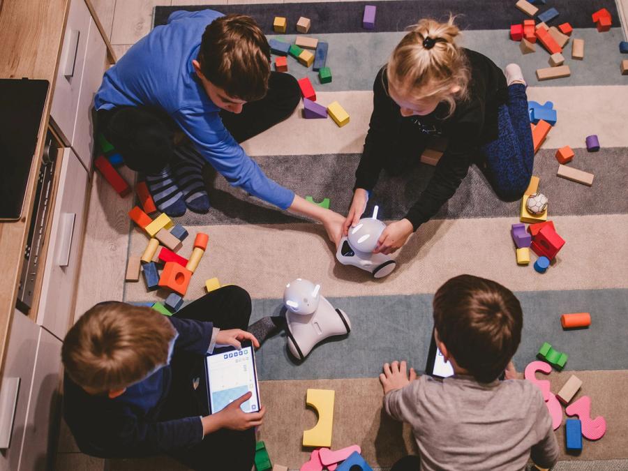 Four children on a school rug play with two Photon robots.