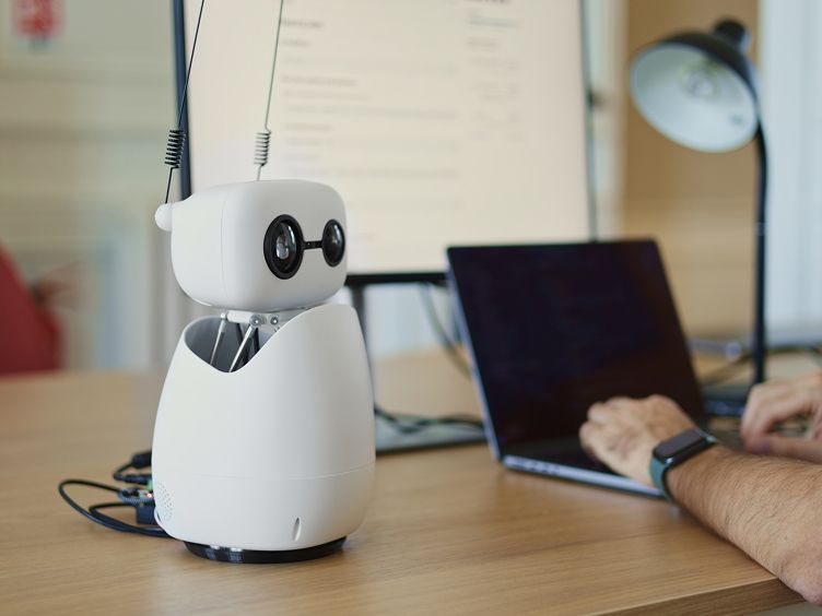 Reachy Mini, a tabletop version of Reachy, has a white head and egg shaped body with two camera eyes, one larger than the other, and two antennae.