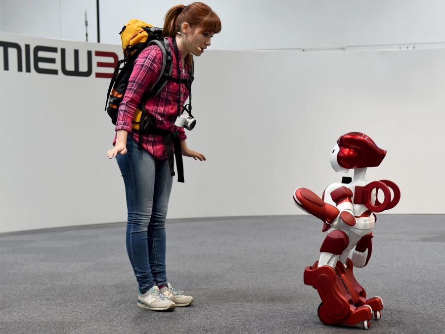 A person with a backpack addresses Emiew, who is half the size of the human.