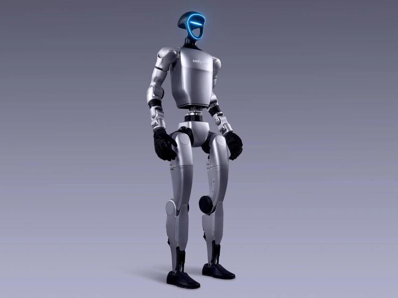 Unitree Robotics' G1 bipedal humanoid robot has two arms ending in black gloved 5 digit hands. It's blue-lit frame shaped face has cameras and sensors.