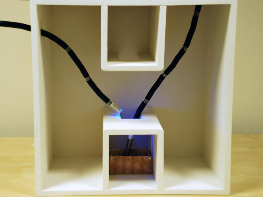 Close-up of two thin, long, black tubes with lights on the end moving into a cube with a hole on top.