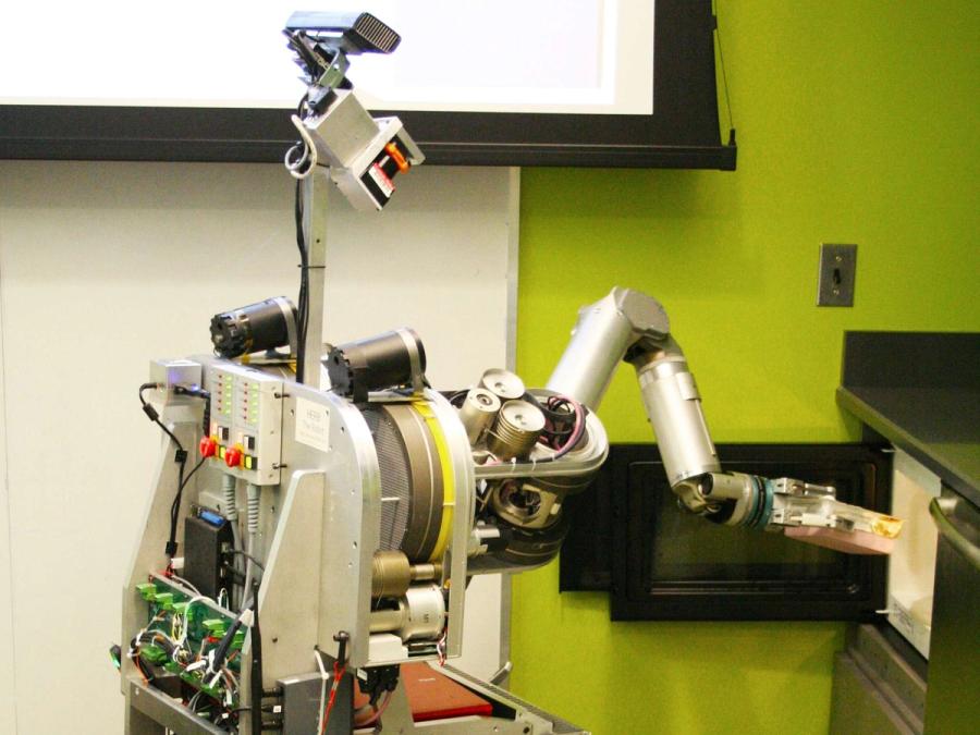 The robot is putting a container in a microwave.