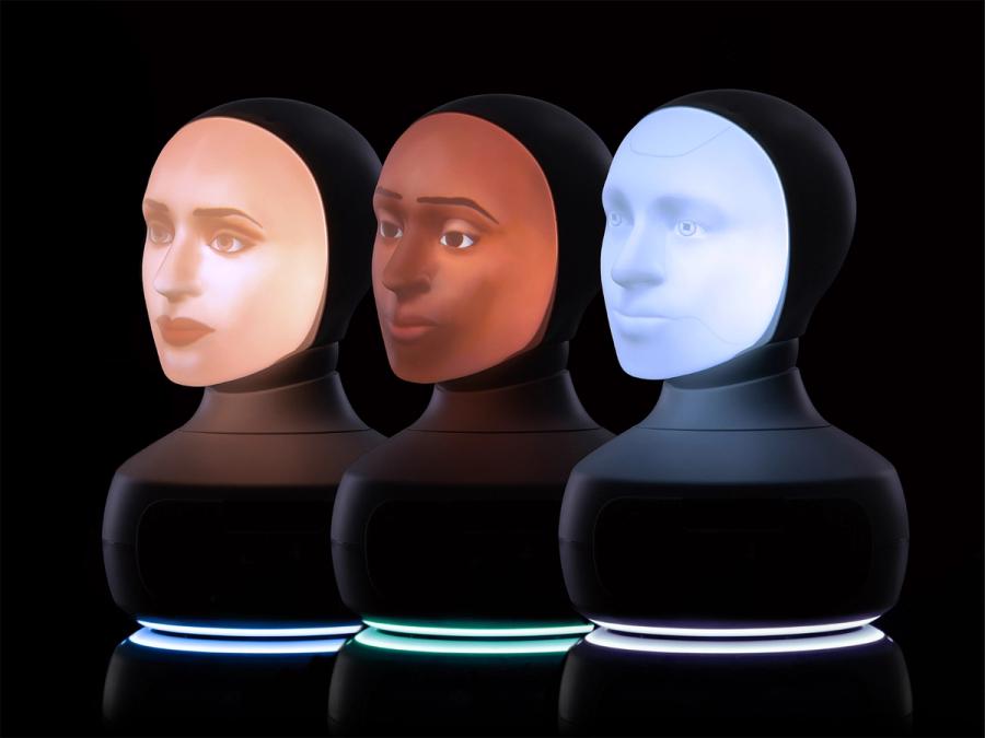 Three tabletop Furhat robots sit in a row. Each consists of a black base with a unique, back projected face.