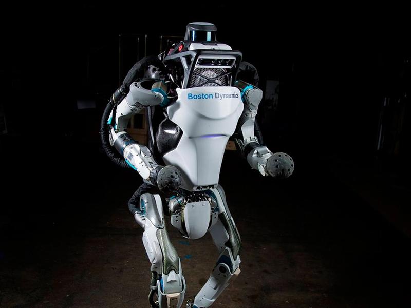 An advanced looking two legged humanoid robot stands on a dark surface.
