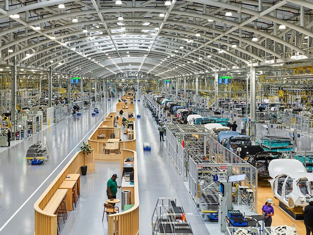 A vast manufacturing hall stretches into the distance, with robotic vehicles visible in the foreground.